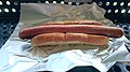 a hotdog made of a slice of toast bread on some aluminium foil. the sausage is both undercookend and burned. there is no seasoning or sauce